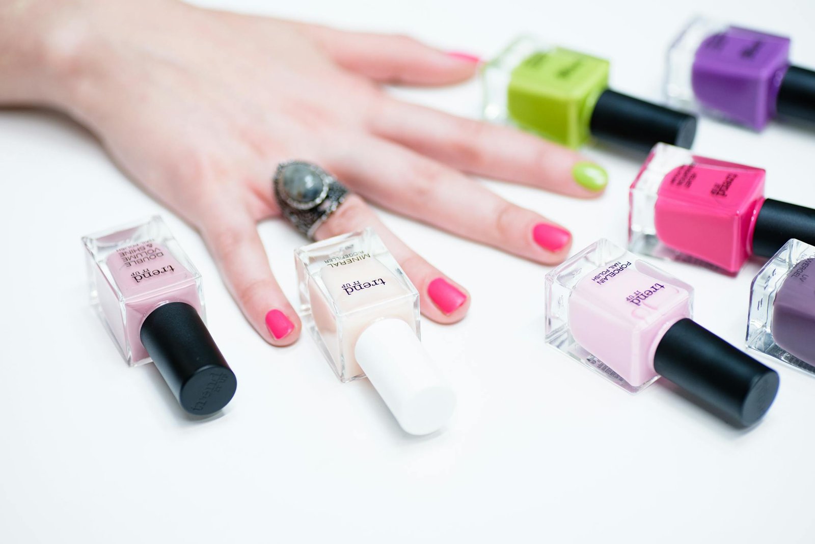 Close-up of a hand with colorful manicure surrounded by various nail polish bottles.