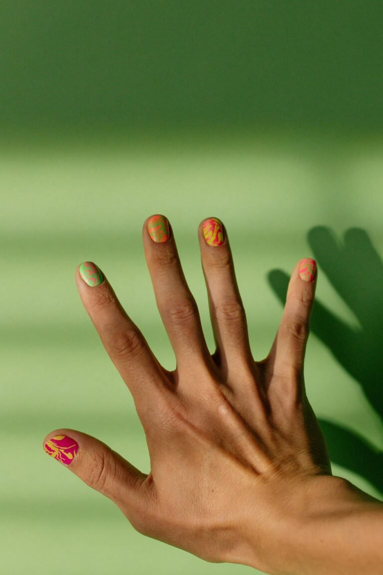 Close-up of a hand with colorful nail art against a green backdrop.