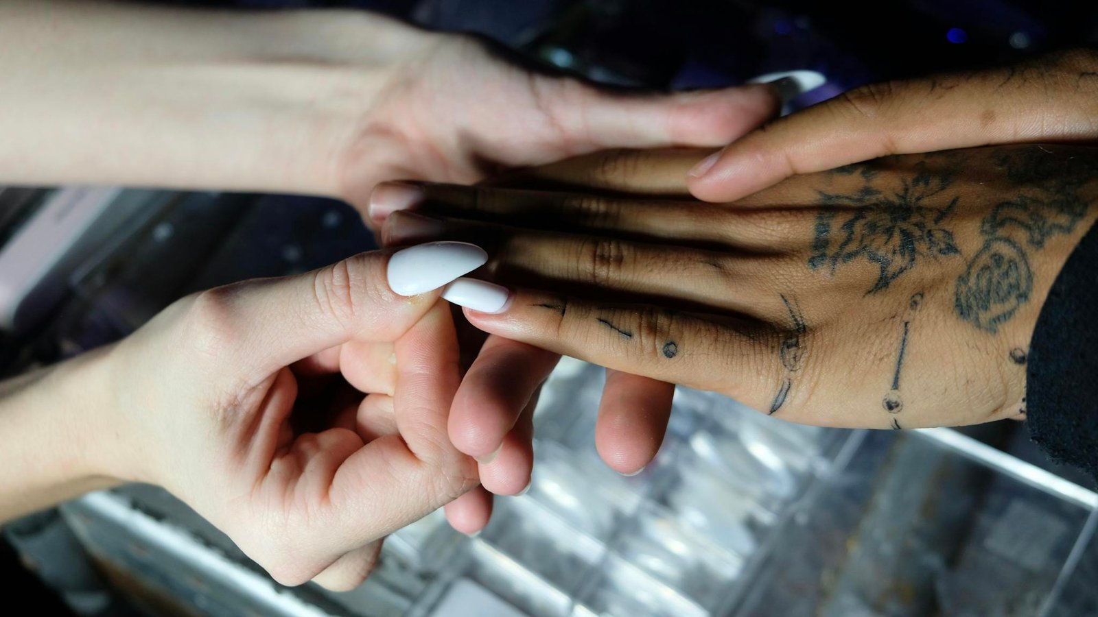 Close-up of nail artist applying manicure to a tattooed hand in a studio setting.